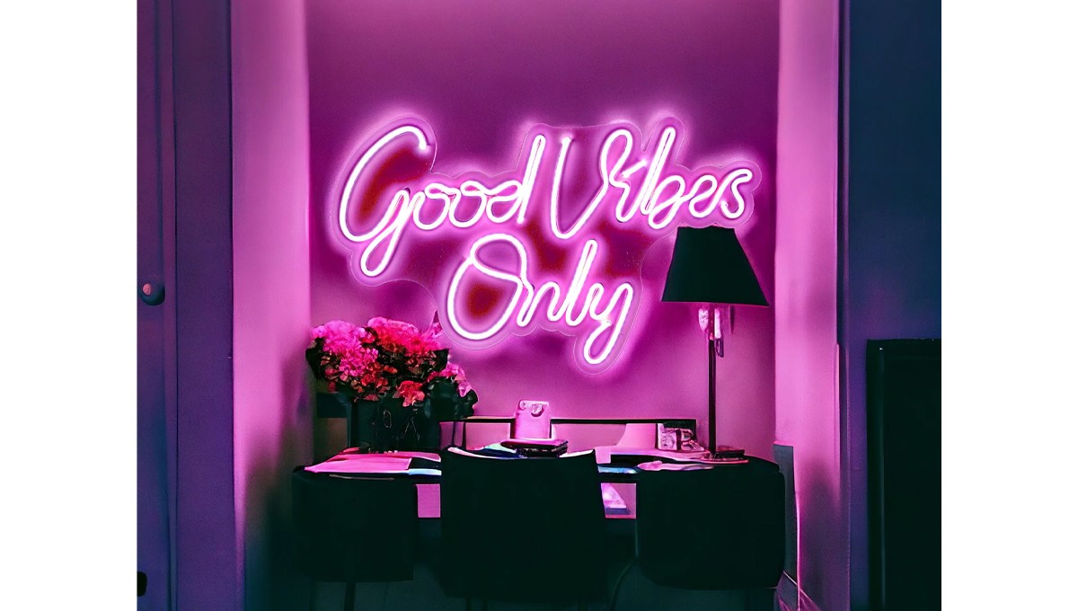 A pink "Good Vibes Only" neon sign on a wall above a desk in a dark room. A pink "Good Vibes Only" neon sign on a wall above a desk in a dark room.